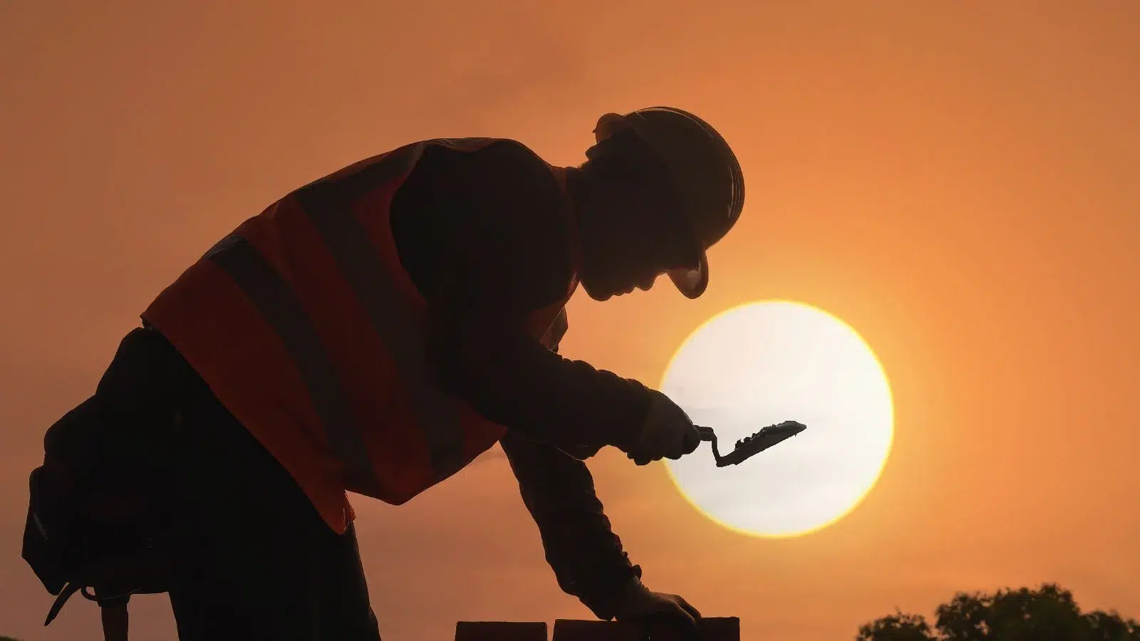 عامل بناء يرتدي معدات السلامة أثناء العمل عند غروب الشمس