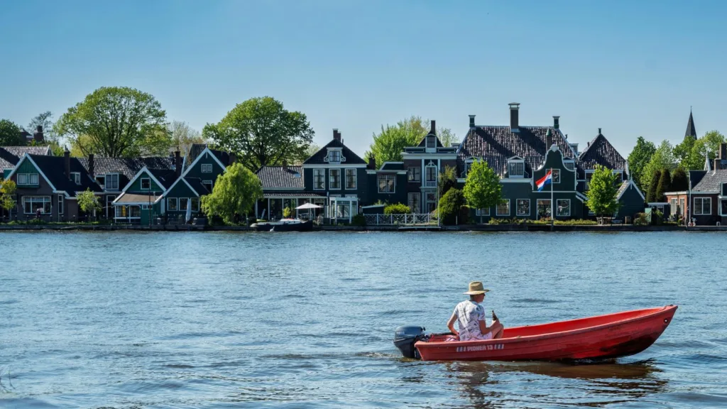 مشهد لمدينة هولندية تقليدية على ضفاف الماء مع منازل تاريخية وقارب صغير، يرمز للحياة والاستقرار في هولندا.